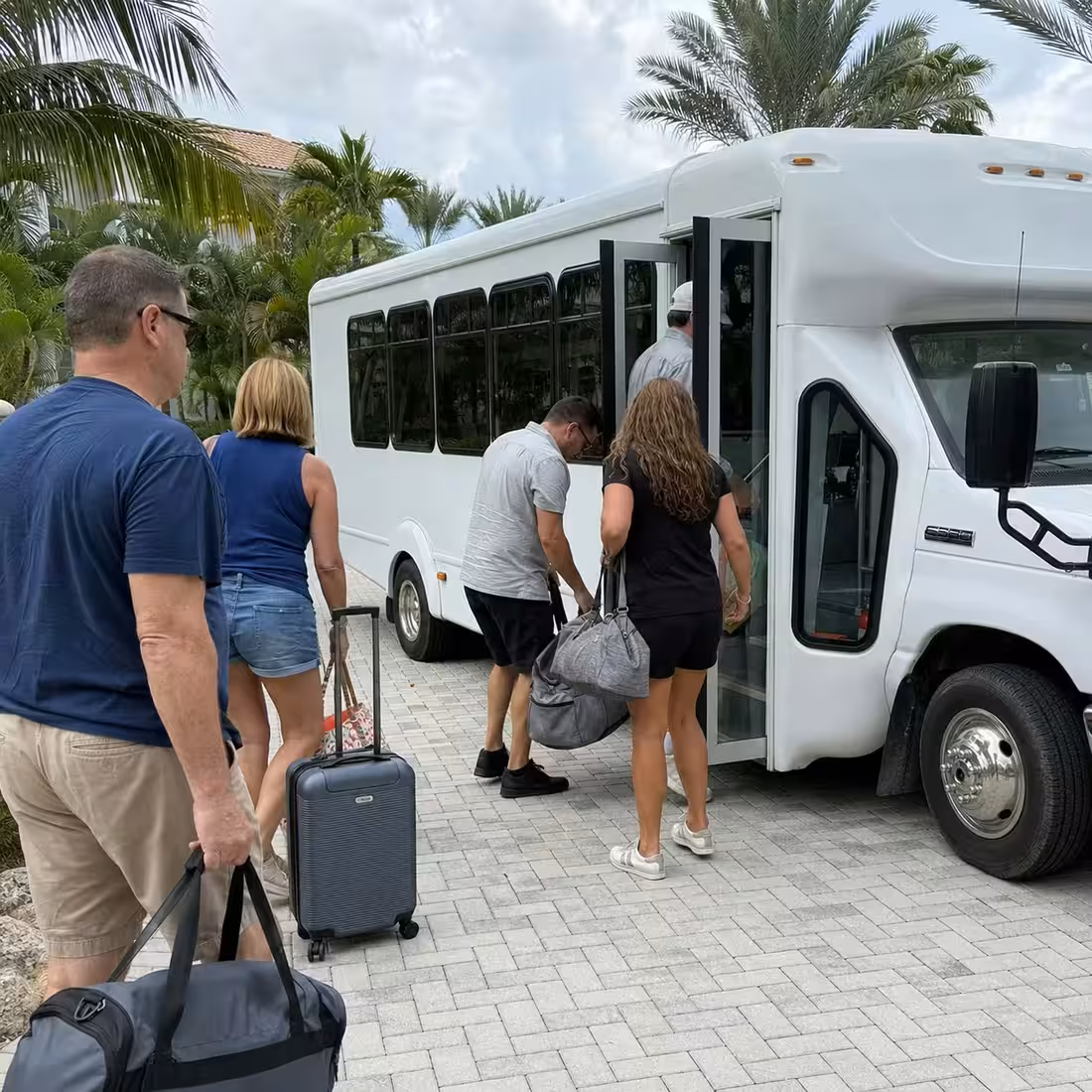 Adults with weekend bags boarding a white minibus shuttle at a Naples Airbnb driveway
