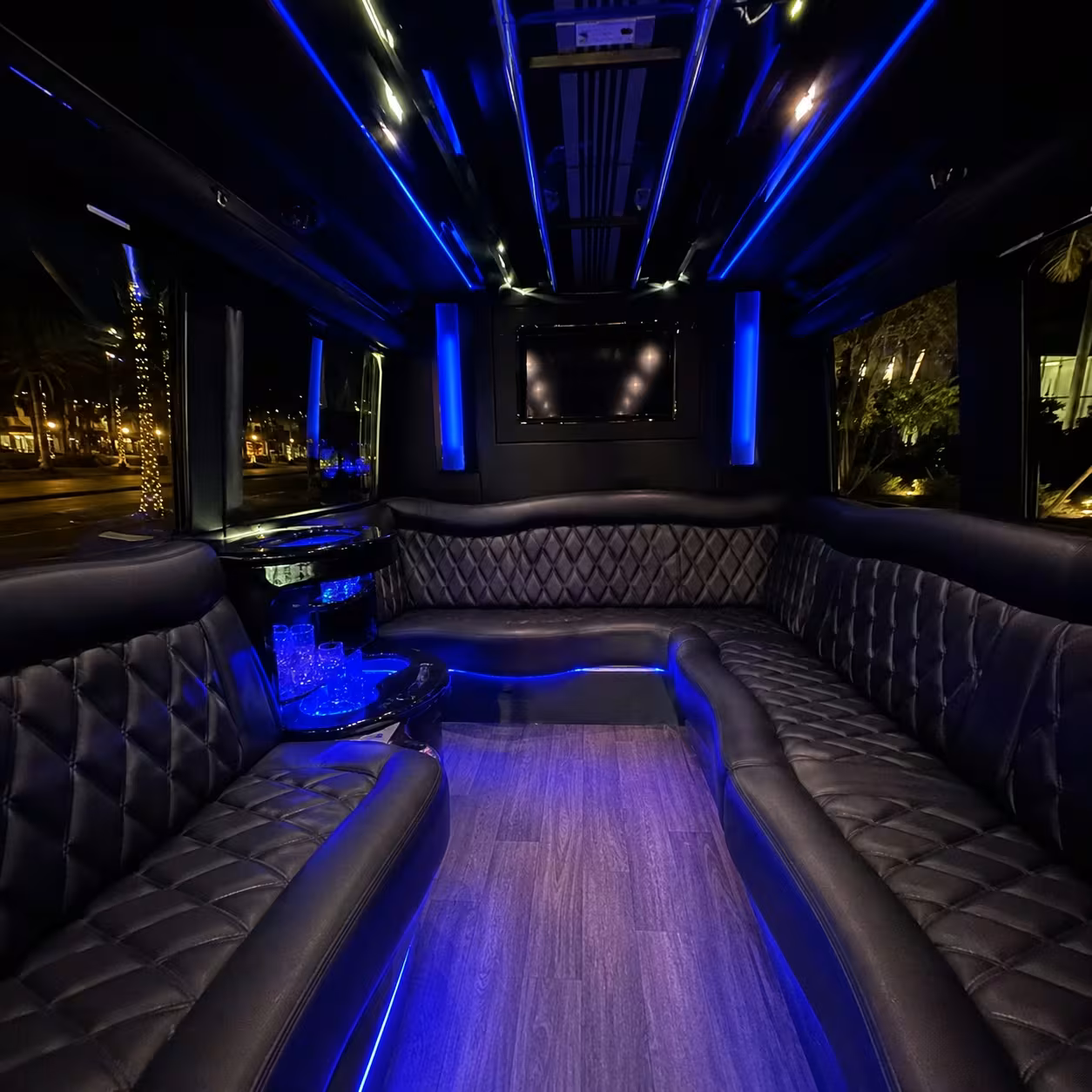 Party bus interior with black leather perimeter seating and blue LED lighting in Naples