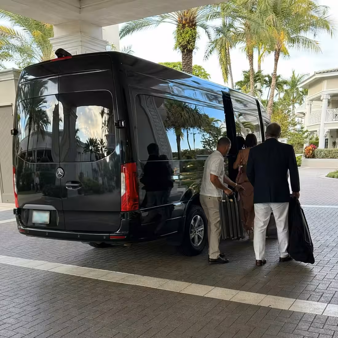 Driver handling luggage as guests board a black Sprinter limo at a Naples beach hotel curb