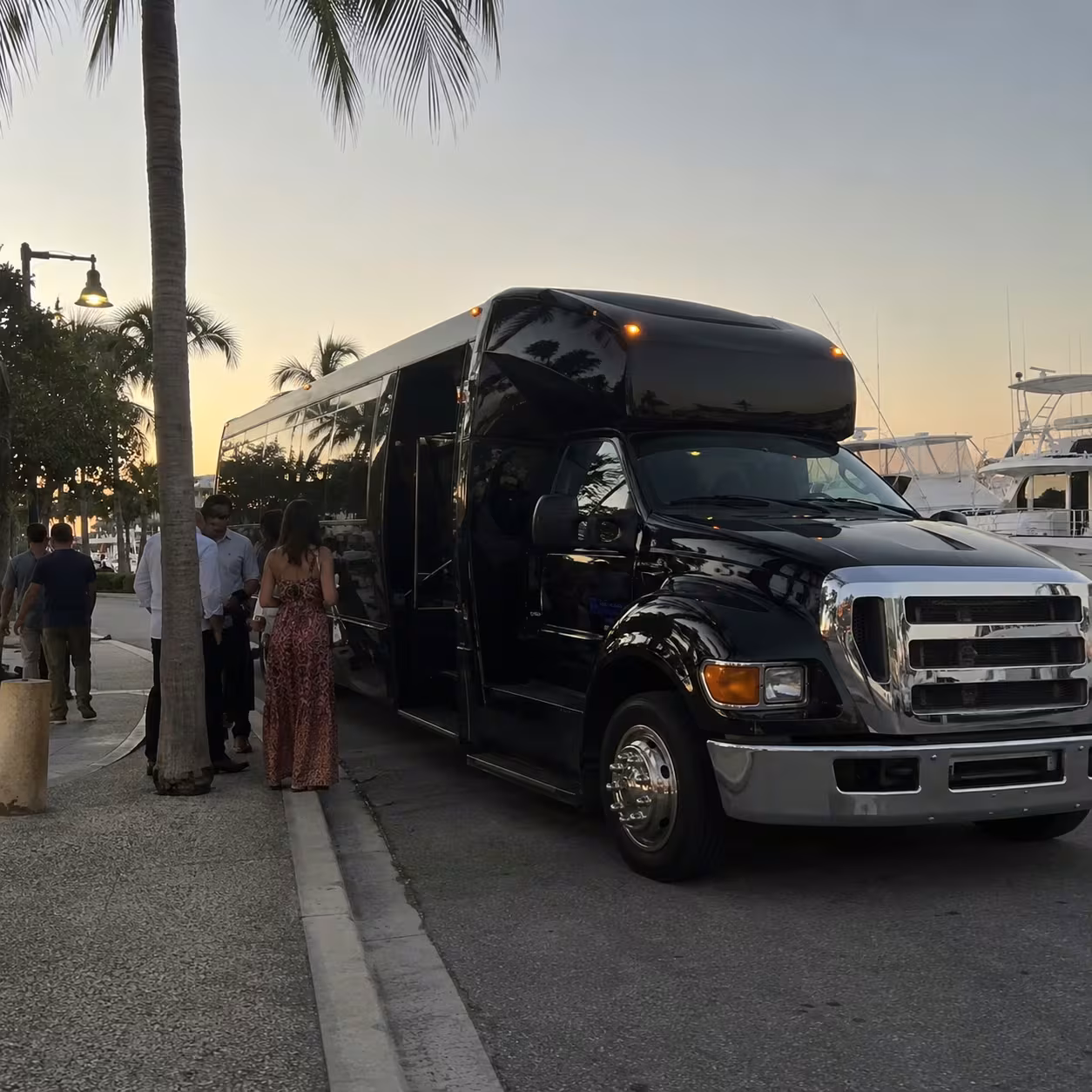 Black party bus parked near a Naples waterfront marina at dusk