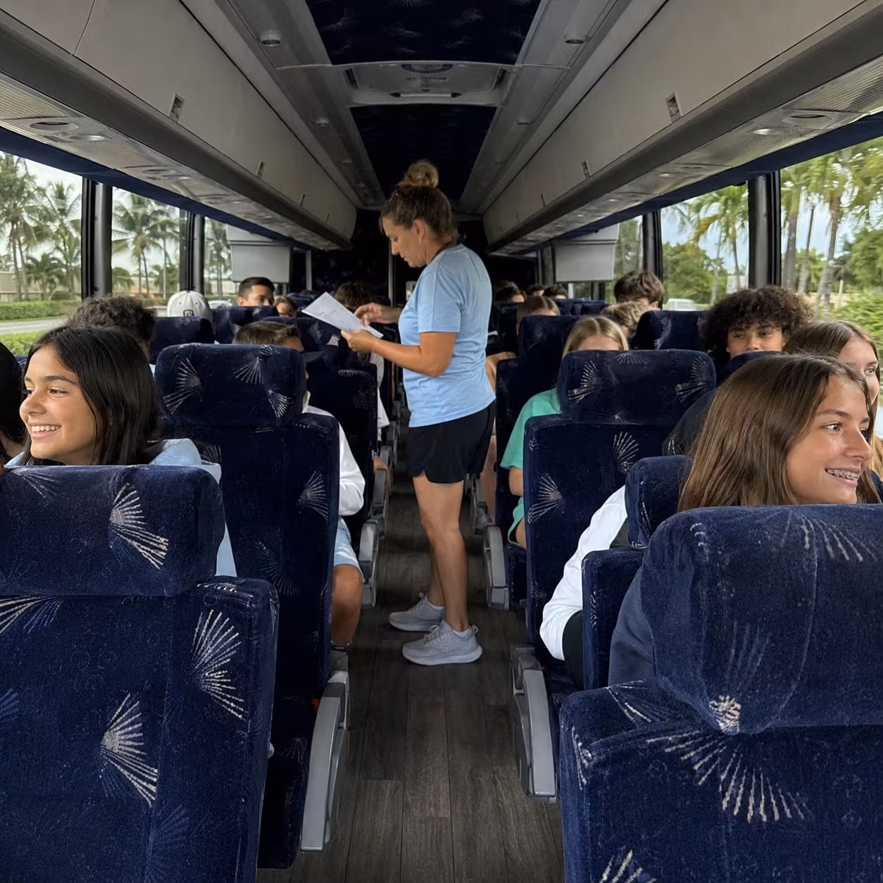 Chaperone checking a roster in the aisle of an MCI J4500 for a Naples school trip